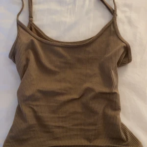 Ljusbrun ribbad linnetopp från Hollister - Säljer en beige ribbad linnetopp från Hollister. Toppen har smala axelband och en åtsittande passform, perfekt för varma dagar. Den är en del av deras Must-Have Collection och är tillverkad i Vietnam.