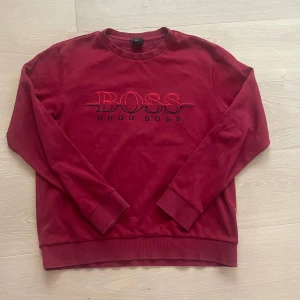Röd sweatshirt från Hugo Boss - Snygg röd sweatshirt från Hugo Boss med deras logga broderad på framsidan. Tröjan har rund hals och långa ärmar, perfekt för alla stilar. Den är gjord i mjukt material som är riktigt bekvämt!