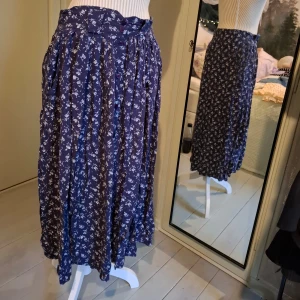 Blommig långkjol från Classic - Säljer en vacker blå långkjol från Classic med ett fint blommigt mönster. Kjolen har knappar framtill och en bekväm passform. Perfekt för en stilfull look.