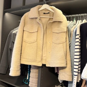 Beige teddyjacka från Gina Tricot - Säljer en mysig beige teddyjacka från Gina Tricot. Jackan har en klassisk krage och två stora bröstfickor. Perfekt för kyliga dagar med sin mjuka och varma känsla. Stängs med knappar framtill.