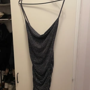 Svart glittrig klänning - Snygg svart klänning med glittrigt mönster och smala axelband. Perfekt för en kväll ute med vänner. Klänningen har en åtsittande passform. Helt ny med prislapp på