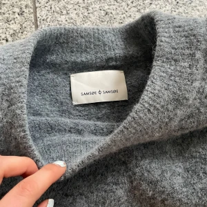 Grå ulltröja från Samsøe Samsøe - Mysig grå tröja från Samsøe Samsøe i ull. Perfekt för kyliga dagar med sin mjuka och varma känsla. Tröjan har en klassisk design med långa ärmar och rund halsringning. Gjord av Både alpacka och merinoull. Köpt second hand men i gott skick