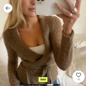Brun omlottkofta med knytband - Säljer en mysig brun omlottkofta med knytband i midjan. Koftan är ribbad och har långa ärmar, perfekt för kyligare dagar. Den har en djup v-ringning och är tillverkad i ett mjukt material.