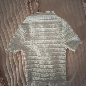 Vit ribbad topp från Divided h&m - Säljer en vit ribbad topp från Divided h&m med korta ärmar. Toppen har en elastisk och texturerad design som ger en unik look. Perfekt för att lägga till en stilfull touch till din garderob.