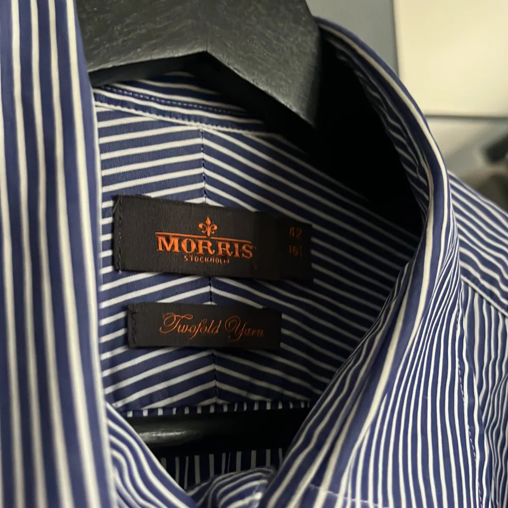 Snygg blå och vit randig skjorta från Morris. Skjortan har långa ärmar och en klassisk krage. Den är broderad med en liten detalj på bröstet och har knappar framtill. Perfekt för en stilren look. Skick 9/10 . Paidat.