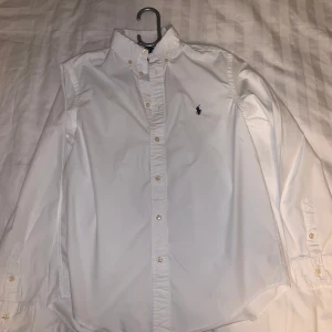 Vit Ralph Lauren polo skjorta - Hej, Säljer nu en stilren vit skjorta från Ralph Lauren polo med broderad logga på bröstet🤩 Skjortan har långa ärmar och knappar framtill perfekt för en stilren look💯 Passar perfekt till finare tillfällen eller vardags🎉🥂(Skriv för fler funderingar, Pris kan även diskuteras‼️)