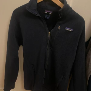 Mörkblå fleecejacka från Patagonia - Tjena! Säljer en mörkblå fleecejacka från Patagonia med dragkedja framtill. Jackan har en broderad logga på bröstet och långa ärmar. Perfekt för kyliga dagar! Fleecen är i bra skick, min bedömning 8-9/10 och har inga defekter. Väldigt klassisk och snygg design som passar till mycket! Nypriset ligger på runt 1699, tveka inte på att höra av dig vid frågor eller funderingar! 