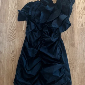 Svart One shoulder klänning med volangdetaljer - Snygg svart klänning med volangdetaljer upptill och en tight passform från Zara. Perfekt för en kväll ute eller en speciell tillställning. Klänningen har en oneshoulder-design som ger en unik look. Står S men skulle säga XS. Endast använd vid ett tillfälle! 