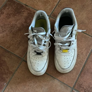 Nike Air Force sneakers i vitt och svart - Säljer ett par Nike Air Force sneakers i vitt med svarta detaljer. Skorna har en klassisk design med snörning och en robust sula. Perfekta för en avslappnad stil.