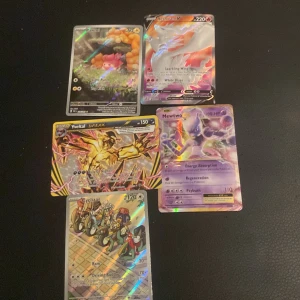 Pokémonkort samling - Säljer en samling av fem Pokémonkort med olika motiv och holografiska effekter. Perfekt för samlare eller spelare som vill utöka sin kortlek. Kortens baksida har den klassiska blå designen med en Pokéball i mitten.