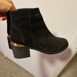 Svarta boots med gulddetaljer från New Look - Snygga svarta boots i mocka med gulddetaljer vid hälen. De har en bekväm klack och en stilren design som passar perfekt till höst- och vintergarderoben.