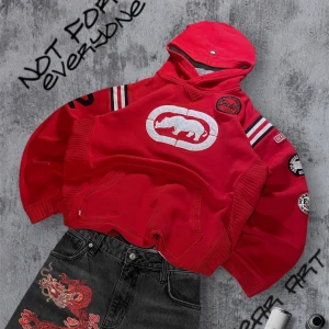 Ecko Unltd Hoodie - Säljer en cool röd hoodie från Ecko Unltd med ett stort vitt noshörningsmärke på framsidan. Tröjan har ribbade muddar och flera märken på ärmarna. Perfekt för en avslappnad stil. storlek M, passar M/L