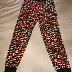 Mönstrade byxor från Kenzo - Snygga byxor från Kenzo med ett iögonfallande mönster i svart, rött och vitt. Byxorna har en elastisk midja och är perfekta för en avslappnad stil. De är tillverkade i ett mjukt material som ger en bekväm passform.