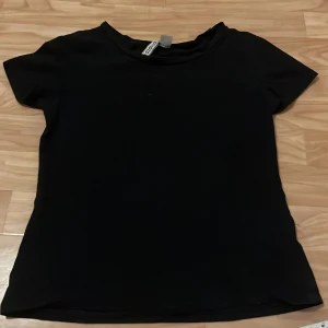 Svart t-shirt från Divided - Säljer en enkel och stilren svart t-shirt från Divided i storlek S! Den har en klassisk rund hals och korta ärmar, perfekt för en avslappnad look. Passar bra till jeans eller kjol.