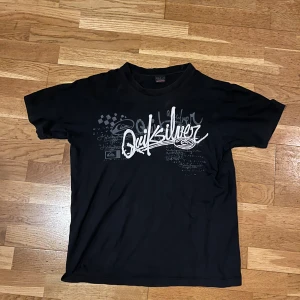 Quiksilver Svart T-shirt - Snygg svart t-shirt från Quiksilver med tryck på både fram- och baksidan. Perfekt för en avslappnad stil. Den har korta ärmar och en klassisk passform.