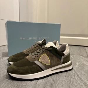  Philippe Model - Snygga gröna sneakers från Philippe Model med detaljer i mocka och syntet. Skorna har en vit sula och snörning framtill. Perfekta för en stilren look.