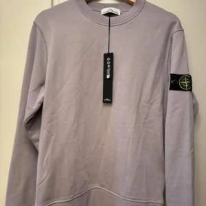 Stone Island tröja - Säljer en stilren grå tröja från Stone Island med deras ikoniska märke på ärmen. Tröjan har en rund hals och långa ärmar. ⚠️ ej autentisk⚠️ strl M