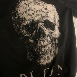 Svart tröja med dödskalle från Philipp Plein - Snygg svart tröja från Philipp Plein med en stor dödskalle i silver på framsidan. Tröjan har en rund halsringning och är dekorerad med små glittriga detaljer. 
