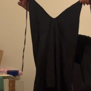 Svart klänning - Elegant svart klänning med smala axelband och en flytande design. Perfekt för en stilren look. Öppen i ryggen