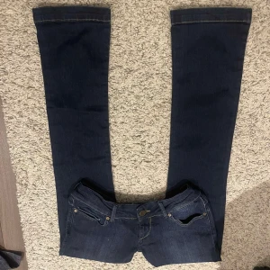 Mörkblå jeans med bootcut - Snygga mörkblå jeans med bootcut-stil. Klassisk femficksdesign och knappgylf. Perfekta för en avslappnad look. Från Cross 🩷