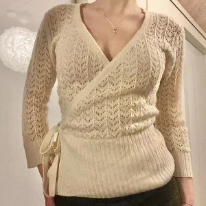 Beige omlottopp med knytband - Säljer ljusbeige omlottopp med v-ringning och knytband i midjan. Toppen har ett fint spetsmönster och trekvartsärmar, mohairblandning!💞
