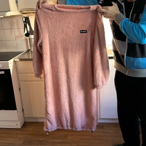 Rosa mysig klänning från So What! - Säljer en supermysig rosa klänning från So What! i fluffigt material. Klänningen har långa ärmar och en avslappnad passform med justerbar nederkant. Perfekt för att mysa hemma eller en chill dag ute. 💖