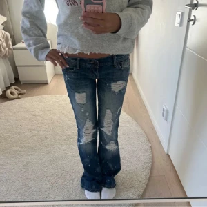 Blå jeans med slitningar från Hollister - Snygga blå jeans från Hollister med slitningar och bootcut-stil. De har en låg midja och klassiska femficksdesign. Perfekta för en avslappnad look.