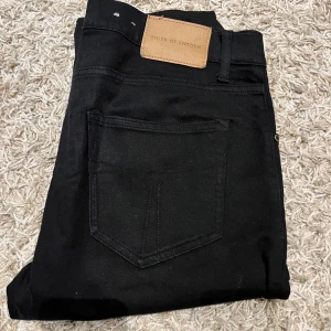 Svarta jeans från Tiger of Sweden - Snygga svarta jeans från Tiger of Sweden med klassisk design. De har en rak passform och är tillverkade i ett slitstarkt material. Perfekta för en stilren look.