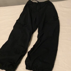 Svarta cargopants med snörning - Säljer ett par svarta cargopants med snörning i midjan och vid bensluten. Byxorna har en loose passform och flera praktiska fickor. Perfekta för en avslappnad stil.