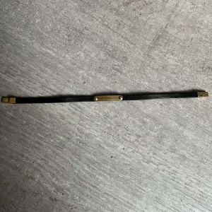 Svart armband från Saint Laurent - Elegant svart armband från Saint Laurent med en diskret guldfärgad detalj i mitten. Armbandet är smalt och stilrent, perfekt för en minimalistisk look. Levereras med originalförpackning och påse. Är öppen för prisförslag!