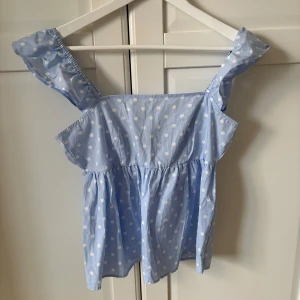 Super söt blå prickig topp med volangdetaljer  - Söt blå topp med vita prickar och volangdetaljer på axelbanden. Toppen har en smockad rygg och en luftig passform. Super fin nu till sommaren och även utomlands 😍