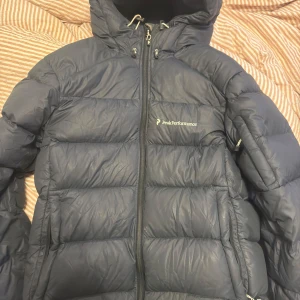 Peak dunjacka  - Peak performance dunjacka. Håller värmen superbra och bekväm luva! Lagad på vissa ställen men inget man tänker på vid användning. Storlek m men passar S med 