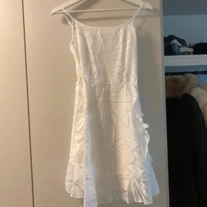 Vit sommarklänning med volangdetaljer - Säljer en superfin vit sommarklänning med tunna axelband och volangdetaljer. Klänningen har ett subtilt mönster och smockad rygg för en bekväm passform. Perfekt för varma sommardagar eller en midsommarfest! 🌸