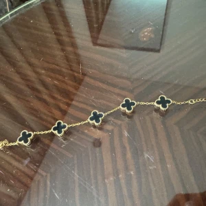 Guldhalsband med fyrklöver - Snyggt guldhalsband med fem svarta fyrklöverberlocker. Perfekt för att ge en elegant touch till din outfit. Kedjan är tunn och smidig, vilket gör den bekväm att bära hela dagen. Passar både till vardags och festliga tillfällen.