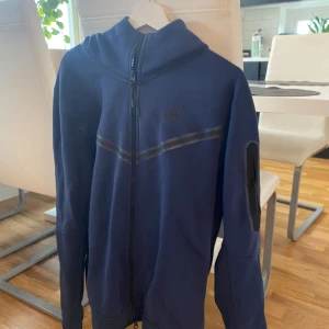 Nike tech fleece tröja - Säljer en snygg blå Nike tech i storlek M. Mitt namn står tyvärr på lappen inuti tröjan. Den har en dragkedja framtill och en praktisk ficka på armen, funkar lika bra till träning som till vardags. Tröjan är i bra skick och redo för nya äventyr! 💙