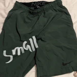 Gröna träningsshorts från Nike - Säljer ett par gröna träningsshorts från Nike i storlek small. De har en elastisk midja för bättre passform och är perfekta för träning. Shortsen är i bra skick och har en liten Nike-logga på benet. Perfekta för sommarens träningspass!