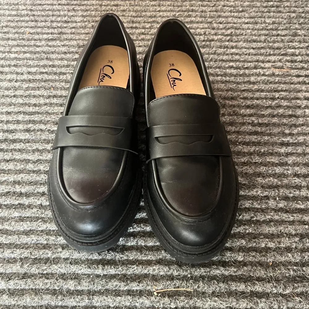 Snygga svarta loafers i skinn, perfekta för både vardag och fest. De har en klassisk design med en bred rem över foten och en robust sula för extra komfort. Skorna är i nyskick och redo att användas direkt. Passar perfekt till både jeans och klänning!. Skor.