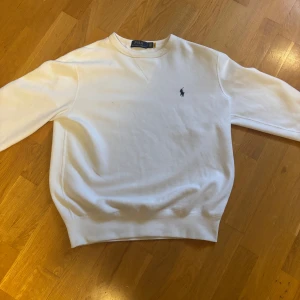 Vit tröja från Ralph Lauren - Säljer en klassisk snygg  vit tröja från Ralph Lauren. Tröjan är i bomull och har en normal passform med långa ärmar. Perfekt för en stilren och avslappnad look. Passar till alla tillfällen! Inga defekter. Skicka Dm vid frågor och intresse 