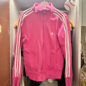 Säljer en snygg rosa träningsjacka från Adidas med vita ränder längs ärmarna. Jackan har dragkedja och två fickor framtill. Perfekt för träning eller som en casual vardagslook. Den är i bra skick och redo för nya äventyr! 🌟