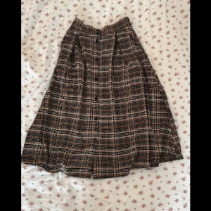 Rutig Långkjol - Rutig långkjol från Monki. Knappar på framsidan, delvis resår i midjan för bättre passform. Fickor på var sida. Silkigt material.