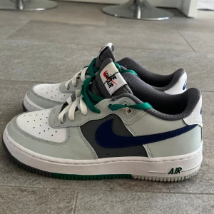 Nike Air Force med gröna skosnören - Säljer ett par klassiska Nike Air Force sneakers i vitt med blå detaljer och gröna skosnören. Skorna har en stilren design med perforerade detaljer på tån för extra ventilation. De är i bra skick och perfekta för både vardag och träning. Toppskick använda två ggr.