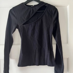 Svart ribbad topp med asymmetrisk design - Säljer en svart ribbad topp med en cool asymmetrisk design. Den har långa ärmar och en unik skärning vid halsen som ger en edgy look. Perfekt för både vardag och fest!