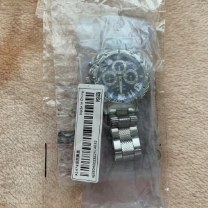 Silverfärgad klocka med metallarmband - Säljer en snygg och robust silverfärgad klocka med ett metallarmband. Klockan har en stor urtavla med flera mindre urtavlor och tydliga siffror. Perfekt för både vardag och fest! 