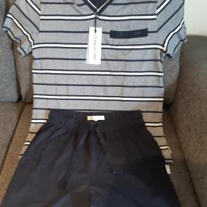 Randig t-shirt från Cerruti 1881 - Säljer ett riktigt snyggt pyjamas set i grå, marinblå och vit färg från Cerruti 1881. T-shirten har en stilren v-ringning och en liten bröstficka med märkeslogga. Marinblåa shorts. Perfekt om du söker en lite snyggare pyjamas. Helt nytt och oanvänt.