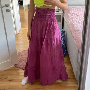 Rosa långklänning - Säljer en superfin rosa långklänning med smockdetaljer upptill. Perfekt för sommarens alla fester eller en mysig dag på stan. Klänningen har en luftig passform och är gjord i ett lätt material som faller snyggt. passar också att ha som långkjol:)