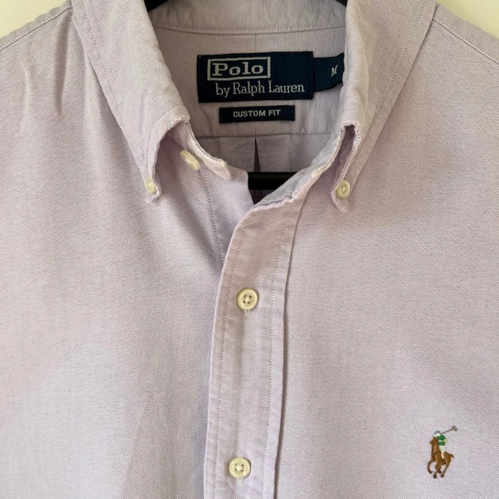 Ljuslila button down-skjorta från Polo Ralph Lauren. Skjortan har ett minimalt hål vid vänster varmbåge, annars är den i bra begagnat skick. Medium till storleken och Custom fit. Tillverkad i 100% bomull. -Ställ frågor! Priset är inte hugget i stenen. Hoodies.