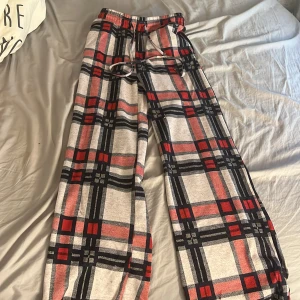 Rutig byxa med snörning - Säljer ett par superbekväma och stiliga byxor med rutig design i svart, röd och vit. De har en loose passform och är perfekta för en avslappnad look. Byxorna har snörning i midjan för justerbar passform.