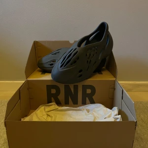 Svarta Adidas Yeezy Foam Runners - Säljer ett par Adidas Yeezy Foam Runners carbon. De är i nyskick och kommer i originalkartong. Skorna har en unik design med många utskärningar för ventilation och en bekväm passform. Perfekta för sommarens alla äventyr!