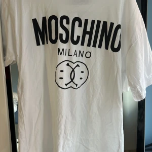 Vit t-shirt från Moschino - Säljer en snygg vit t-shirt från Moschino med stort tryck på framsidan. Den har en klassisk rund hals och korta ärmar. Perfekt för en casual look eller att styla upp med accessoarer. T-shirten är i bra skick och redo för nya äventyr!