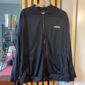 Adidas svart zip-up tröja  - Helsvart Adidas-tröja med dragkedja/zip-up. Glansiga detaljer på fickor (inga dragkedjor) och glansiga 3 stripes på ärmarna. I mycket gott skick! Kan frakta eller mötas upp i Stockholm eller Uppsala.